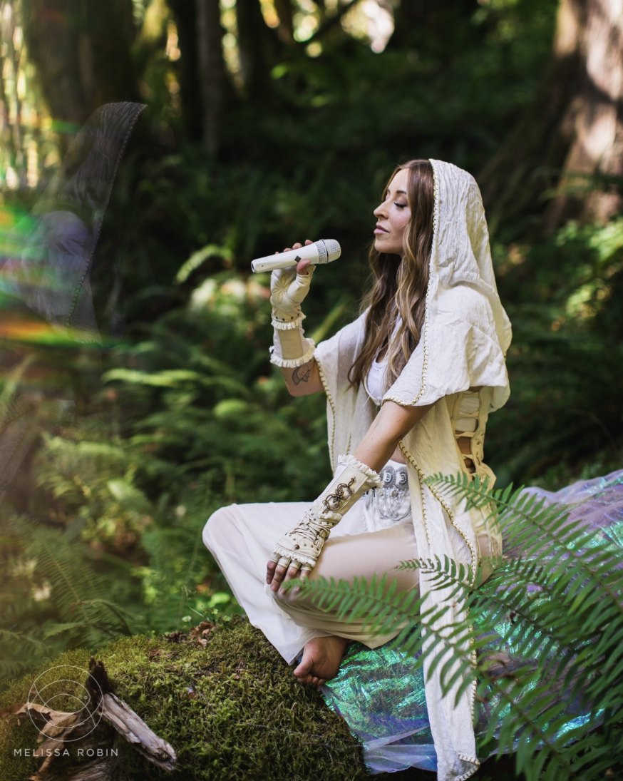 Leanne seated on moss among ferns, singing softly into a microphone