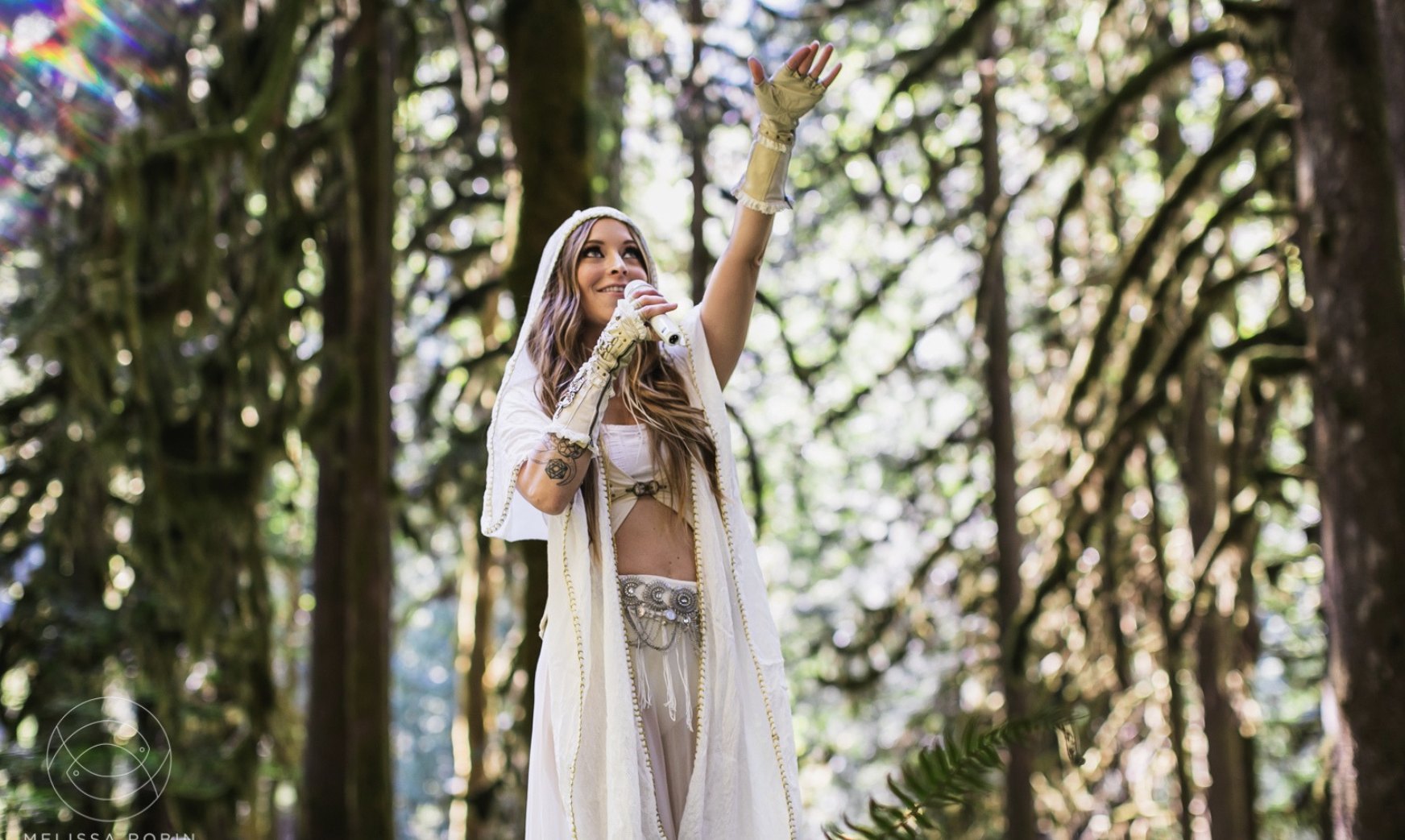 Ayaharmony singing into a microphone in a sunlit forest, one arm raised to the sky