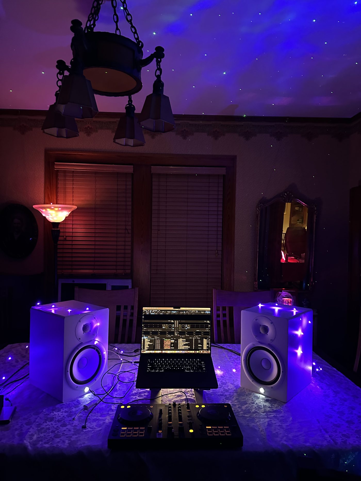 Leanne's DJ setup glowing violet: a controller, laptop and two white monitor speakers wrapped in fairy lights, with stars projected on the ceiling