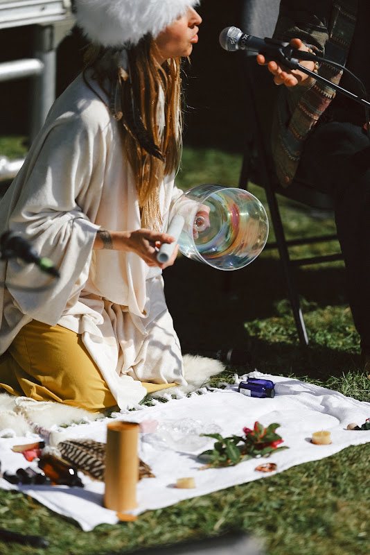 Leanne kneeling beside her altar playing an iridescent crystal singing bowl