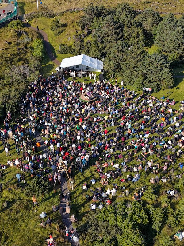 Aerial view of a huge crowd gathered on a green hillside around the festival tent