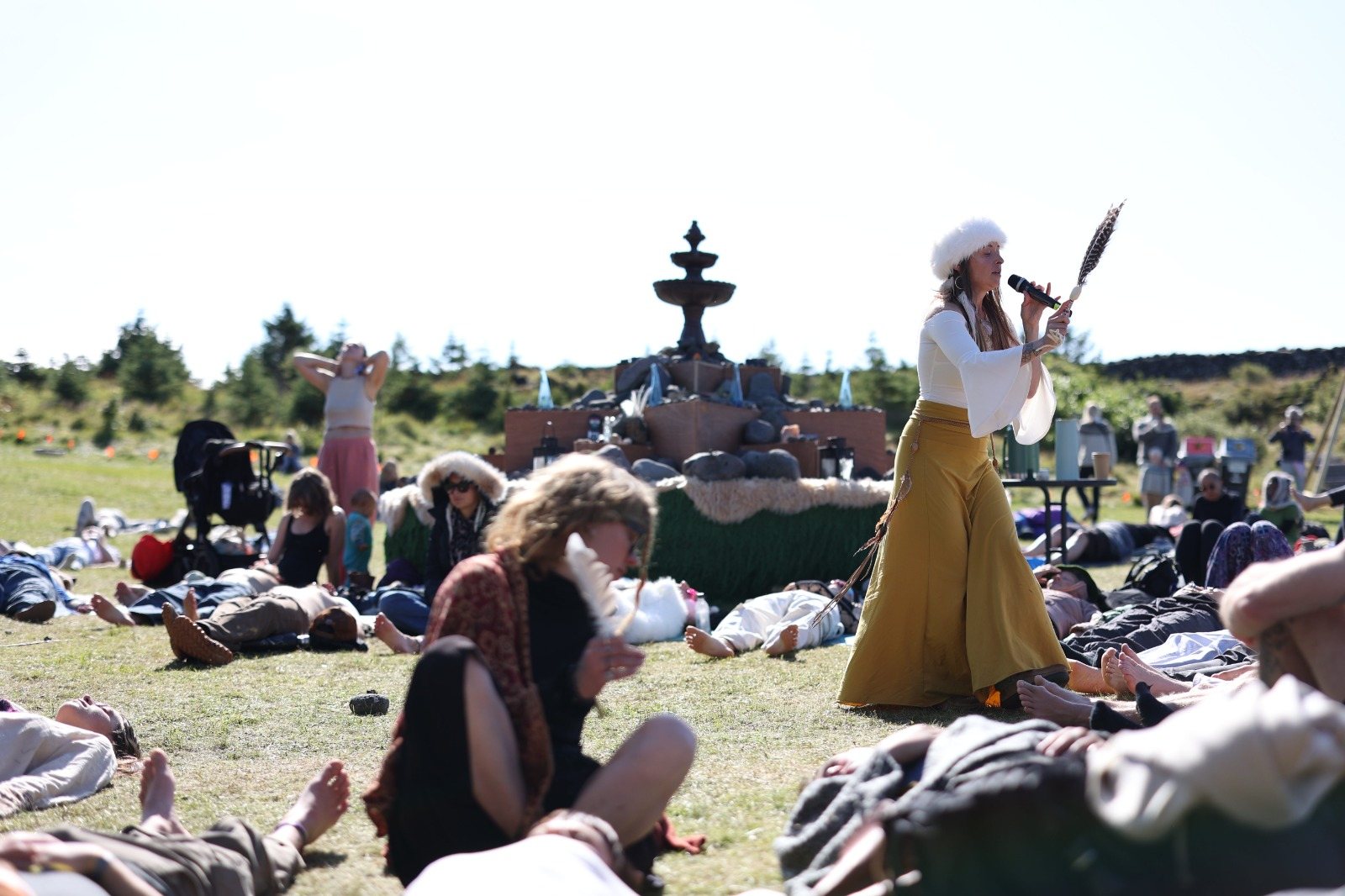 Leanne walking through the resting crowd singing, feather in hand, before the stone fountain