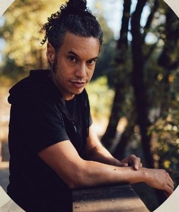 Mos Jef leaning on a wooden railing among trees